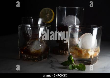 plusieurs verres à whisky remplis de différentes couleurs infusées de vin de gin au rhum vodka boissons avec des boules de glace et des quartiers de lime, menthe montrant le Banque D'Images