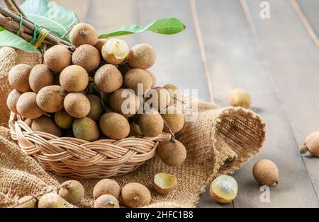 Fruits de longan frais avec feuilles dans un panier de bambou sur fond de bois, fruits d'Asie Banque D'Images