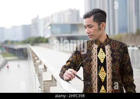 Un jeune modèle masculin habillé en indonésien Batik avec le motif de fleur balinais tenant des lunettes de soleil au long Museum, West Bund, Shanghai Chine Banque D'Images