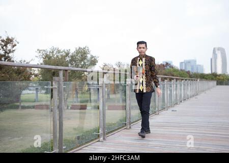 Un jeune modèle masculin vêtu de Batik indonésien avec un motif floral balinais marche au long Museum, West Bund, Shanghai en Chine Banque D'Images