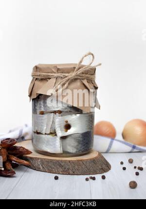 Harengs marinés, poivre et épices dans un pot sur la table, fond clair, photo verticale Banque D'Images