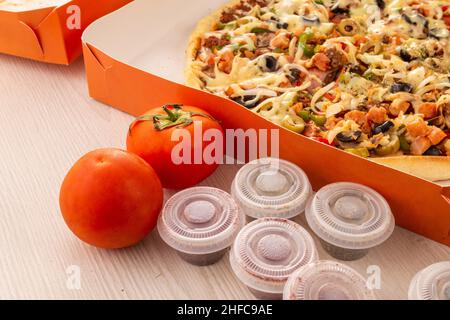 emballage en carton avec une délicieuse pizza sur une table à côté de quelques tomates décorant et des contenants avec origan, fast food et style de vie Banque D'Images