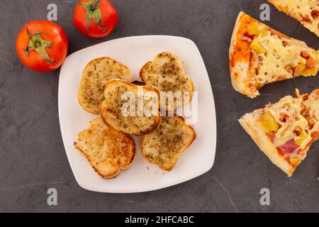 cuisine en studio détail de l'assiette avec pain à l'ail et pizza avec fromage, ananas et jambon, décoration avec tomates, table réservée et prête à manger Banque D'Images