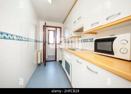 Cuisine meublée d'un côté de la chambre avec mobilier blanc, comptoir couleur bois clair et bordure bleue Banque D'Images