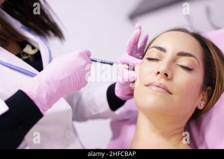 Médecin injectant de l'acide hyaluronique dans les pommettes d'une femme comme traitement de rajeunissement facial. Banque D'Images