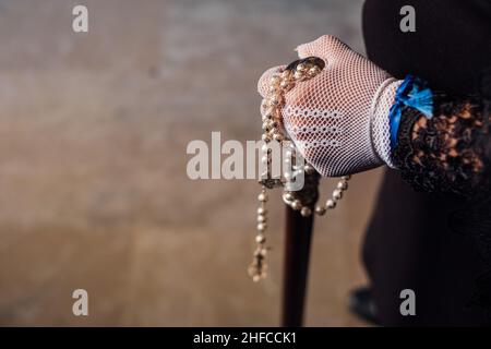 Femme habillée en costume traditionnel andalou de Pâques tient un rosaire et une photo de Jésus dans sa main le long d'une rue typique de Grenade Banque D'Images