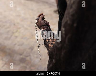 Femme habillée en costume traditionnel andalou de Pâques tient un rosaire et une photo de Jésus dans sa main le long d'une rue typique de Grenade Banque D'Images