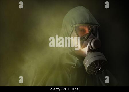 Un homme dans un costume de protection vert et un masque à gaz marche à travers la fumée toxique.Portrait en demi-longueur. Banque D'Images