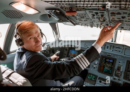 Un pilote mâle appuie sur le bouton du panneau de pavillon dans le cockpit de l'avion Banque D'Images