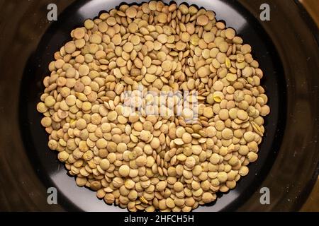 Lentilles vertes biologiques non cuites dans un plat en céramique noire, macro, vue du dessus. Banque D'Images