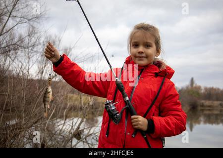 Petite fille dans une veste rouge avec un poisson dans ses mains Banque D'Images