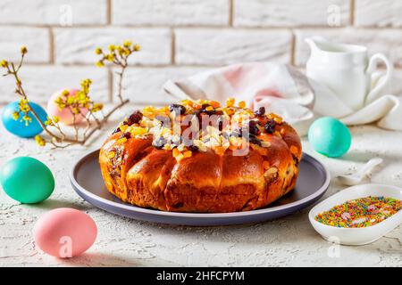 couronne de pain de pâques parsemée de morceaux d'orange confits, de raisins secs et de tranches d'amandes pelées sur une assiette sur une table avec une branche en fleur, de couleur par exemple Banque D'Images