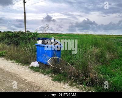 Poubelle débordante sur le côté de la route dans le village.Nettoyage et élimination des ordures dans les bâtiments résidentiels. Banque D'Images