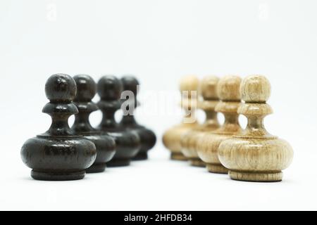Pions d'échecs blancs et noirs en bois isolés les uns devant les autres sur fond blanc.Concept de jeu d'échecs. Banque D'Images