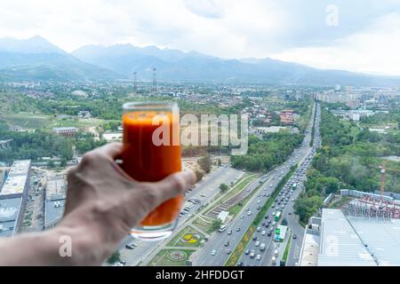 Main tenant jus de carotte avec la vue de dessus de l'avenue menant à Almaty montagnes, Kazakhstan Banque D'Images