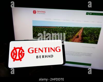 Personne tenant un téléphone portable avec le logo du groupe de Genting de Malaisie (Berhad) à l'écran devant la page Web.Mise au point sur l'affichage du téléphone. Banque D'Images