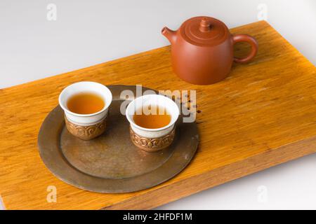 Théière en céramique et trois tasses traditionnelles pour boire du thé oriental sur une table en bois pour les cérémonies du thé sur fond blanc.Les tasses sont remplies de wi Banque D'Images