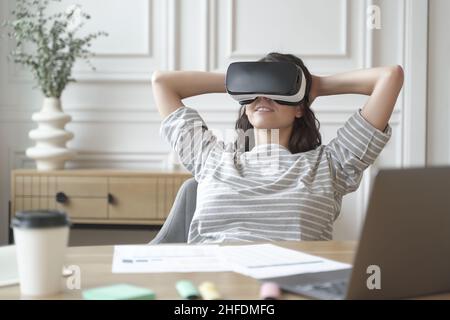 Jeune femme de bureau détendue dans un casque VR ou un casque regardant dans une vidéo ou un film à 360 degrés Banque D'Images