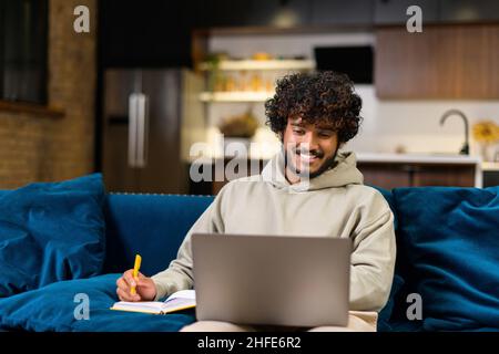 Travailleur indépendant hindou multiethnique utilisant un ordinateur portable pour travailler ou étudier à distance de la maison.Homme indien concentré regardant un webinaire en ligne et prenant des notes dans un ordinateur portable, e-learning Banque D'Images