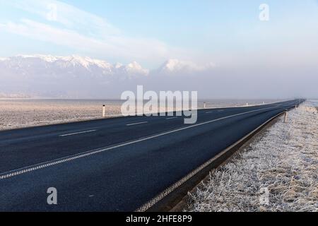 La route vide et la neige couvraient les sommets des Alpes Kamnik–Savinja qui s'enrairaient du brouillard lors du gel du matin, Menges, Slovénie Banque D'Images