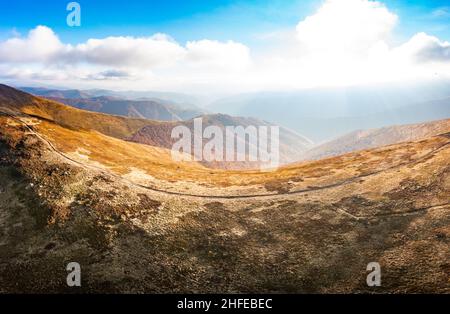 De longues allées étroites longeant la crête de haute montagne sous des nuages blancs moelleux flottant sur le ciel bleu sur une vue aérienne de jour ensoleillé Banque D'Images