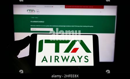 Personne tenant un téléphone portable avec le logo de la compagnie aérienne Italia Trasporto Aereo S.p.A. (ITA Airways) à l'écran en face de la page Web.Mise au point sur l'affichage du téléphone. Banque D'Images