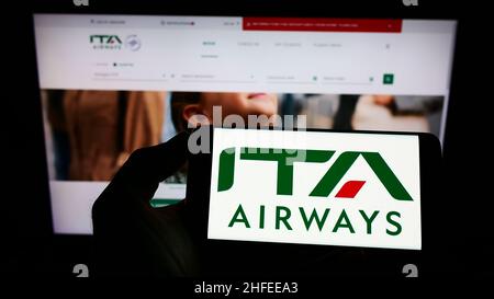 Personne tenant un téléphone portable avec le logo de la compagnie aérienne Italia Trasporto Aereo spa (ITA Airways) à l'écran en face de la page web.Mise au point sur l'affichage du téléphone. Banque D'Images