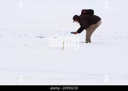 Pêche d'hiver depuis la glace sur le lac (réservoir) par temps froid. Pêcheurs âgés chaleureusement habillés Banque D'Images