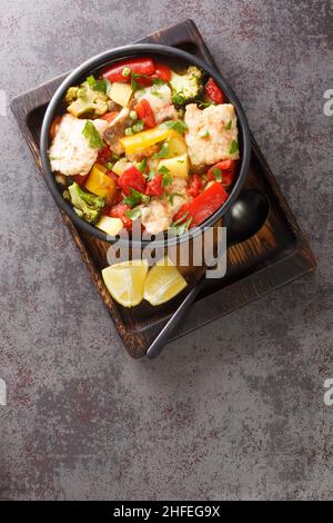 Soupe de poisson épaisse avec poivrons, pommes de terre, petits pois, oignons, brocoli et tomates, vue rapprochée dans un bol sur la table. Vue verticale du dessus Banque D'Images