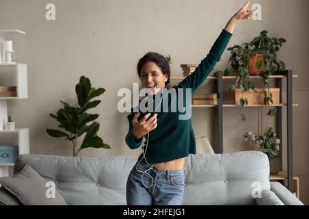 Une femme millénaire joyeuse dansant, tenant son smartphone entre les mains. Banque D'Images