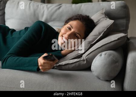 Joyeuse femme détendue regardant la télévision seule à la maison. Banque D'Images