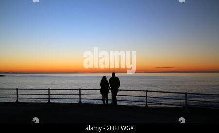 Aberystwyth, pays de Galles, Royaume-Uni - 14-Jan-2022 - deux personnes regardent la lueur du coucher de soleil à Aberystwyth, pays de Galles, Royaume-Uni, alors qu'une période de haute pression apporte un climat calme et stable au Royaume-Uni - photo Credit: John Gilbey Banque D'Images