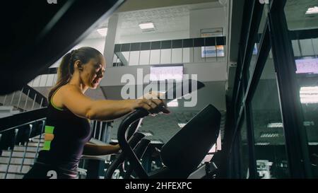 FIT Athletic Woman s'exerçant sur une machine elliptique. Activité musculaire pour les femmes entraînement dans la salle de gym moderne. Les sportifs s'entraînent dans un club de fitness elliptique. Faites de l'exercice au ralenti Banque D'Images