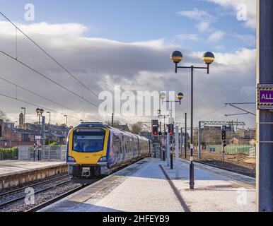 Un train s'éloigne d'une station de chemin de fer, recouverte d'une légère poussière de neige.Les maisons sont en arrière-plan et un ciel nuageux est au-dessus. Banque D'Images