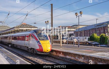 Un train se trouve à la plate-forme d'une gare avec une légère poussière de neige.Les bâtiments sont en arrière-plan et un ciel avec des nuages de lumière est au-dessus. Banque D'Images