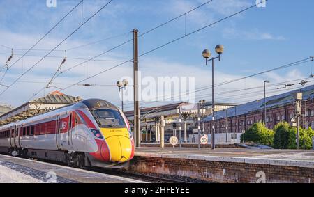 Un train se trouve à la plate-forme d'une gare avec une légère poussière de neige.Les bâtiments sont en arrière-plan et un ciel avec des nuages de lumière est au-dessus. Banque D'Images