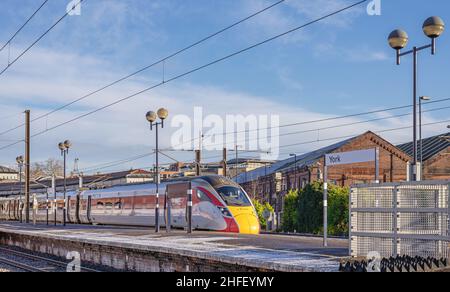 Un train se trouve à la plate-forme d'une gare avec une légère poussière de neige.Les bâtiments sont en arrière-plan et un ciel avec des nuages de lumière est au-dessus. Banque D'Images