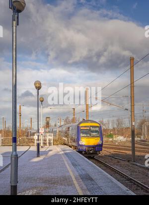 Un train s'éloigne d'une station de chemin de fer, recouverte d'une légère poussière de neige.Un lampadaire est au premier plan et un ciel nuageux est au-dessus. Banque D'Images