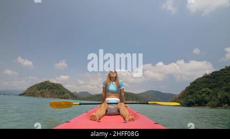 La femme sportive rogue le canoë en plastique rose le long de l'eau de mer. Positive sports girl rembourrage de la main sur le kayak, vue de face. Banque D'Images