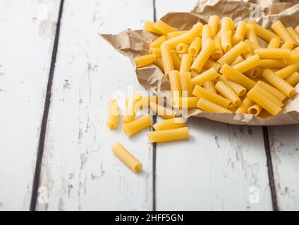 Pâtes de penne maison crues en papier brun sur fond de bois blanc.Macro Banque D'Images