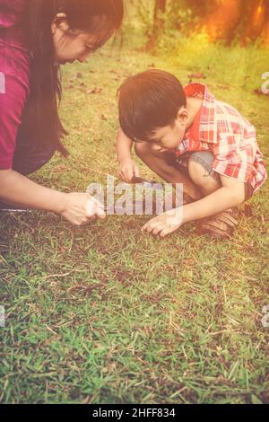 Mère asiatique et beau fils appréciant dans la nature.Jeune garçon explorant la nature au sol avec une loupe. Enfants jouant à l'extérieur avec la lumière du soleil an Banque D'Images