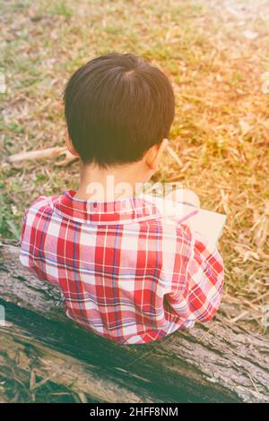 Vue arrière.Enfant utilisez le stylo pour écrire sur le livre dans le parc.À l'extérieur, en journée, en plein soleil.Les enfants lisent et étudient, concept d'éducation.Chaud t Banque D'Images