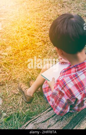 Vue arrière.Enfant utilisez le stylo pour écrire sur le livre dans le parc.À l'extérieur, en journée, en plein soleil.Les enfants lisent et étudient, concept d'éducation.Chaud t Banque D'Images