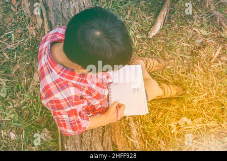 Vue de dessus.Enfant utilisez le stylo pour écrire sur le livre dans le parc.À l'extérieur, en journée, en plein soleil.Les enfants lisent et étudient, concept d'éducation.Chauffer à Banque D'Images