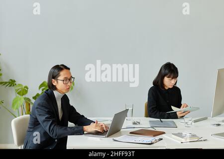 Portrait minimal de deux jeunes gens d'affaires asiatiques utilisant des ordinateurs dans un bureau moderne, espace de copie Banque D'Images
