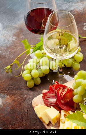 Verres à vin blanc et rouge, planche à raisins et hors-d'œuvre avec fromage et prosciutto Banque D'Images