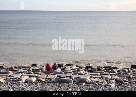 Penzance, Cornwall, 16th janvier 2022, deux personnes profitent du soleil glorieux et se sont assis sur des rochers en regardant la mer calme un dimanche matin à Penzance, Cornwall.Tout le long de la promenade, les gens marchaient, s'asseyant, pédalant et marchant avec des chiens.Les prévisions météorologiques sont pour des conditions ensoleillées et douces au cours des prochains jours.Crédit : Keith Larby/Alay Live News Banque D'Images