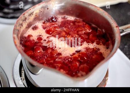 Gros plan de l'ébullition du compote de cerises dans le pot de réserve sur la cuisinière électrique près du comptoir gris Banque D'Images