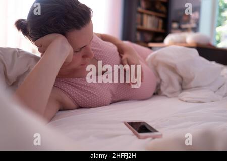 Femme caucasienne avec le téléphone ayant des contractions de travail sur le canapé à la maison et la respiration Banque D'Images