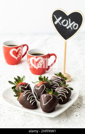 Gros plan de fraises enrobées de chocolat, avec des tasses de café derrière. Banque D'Images